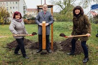 Kerstin Beyer und Sibylle Scheffler schippen Erde auf den frischgepflanzten Baum. Daniel Ruft präsentiert das Namensschild.