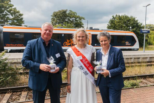 Drei Menschen (Staßfurts Bürgermeister René Zok, die Staßfurter Salzfee und Ministerin Lydia Hüskens) stehen am Bahngleis. Im Hintergrund ist ein Zug im neuen Landesdesign zu sehen