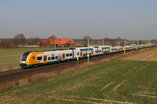 Ein grün-gelb weißer Zug des Typs DESIRO HC der Ostdeutschen Eisenbahn fährt in herbslicher Landschaft.