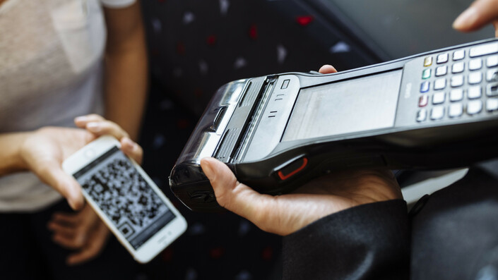 A train attendant's mobile ticket reader scans the QR code of a ticket on a smartphone.