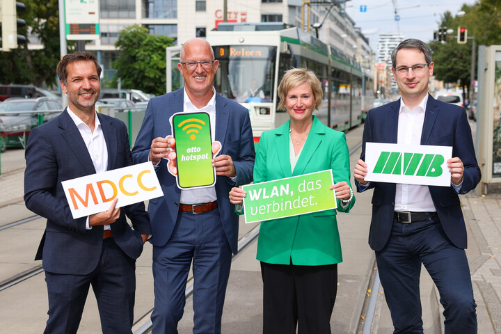 Drei Männer und eine Frau (Patrick Irmer, Guido Nienhaus, Cornelia Muhl-Hünicke und Axel Reinicke) stehen vor einer Straßenbahn und halten Schilder mit den Texten: `MDCC´, `otto hotspot´, `WLAN, das verbindet´ und `MVB´.