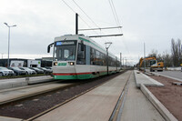 Eine Straßenbahn der Magdeburger Verkehrsbetriebe steht an einer Haltestelle am August-Bebel-Damm. Ein Bagger arbeitet an der Haltestelle der Gegenrichtung.