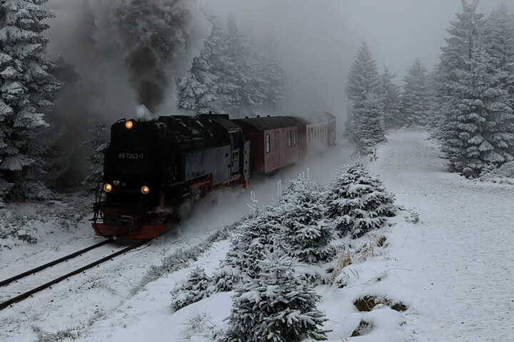 Eine Dampflokomnotive fährt durch eine verschneite bergige Landschaft