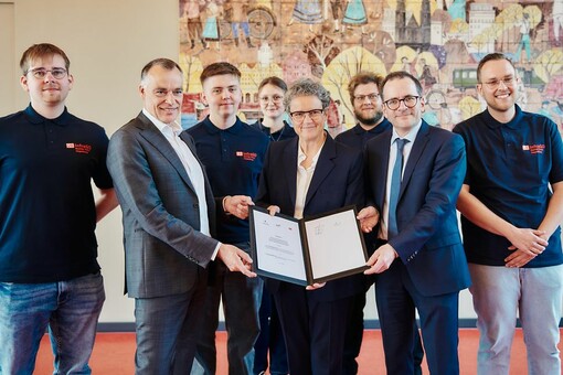 Lydia Hüskens, Peter Panitz und Bernhard Huber halten einen Vertrag. Sie sind umring von Auszubildenden 
