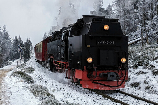 Eine Dampflokomnotive fährt durch eine verschneite bergige Landschaft