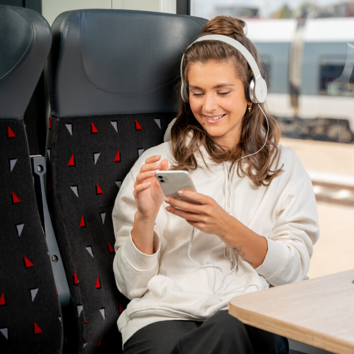 A young woman sits on the train and happily looks at her smartphone.